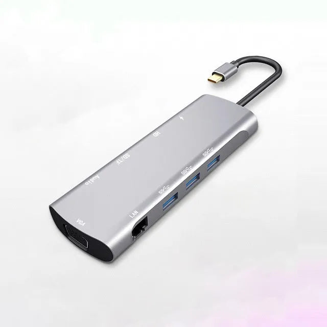 Grey aluminium USBC docking station with HDMI, VGA, USB 3.0, and charging ports on a desk.