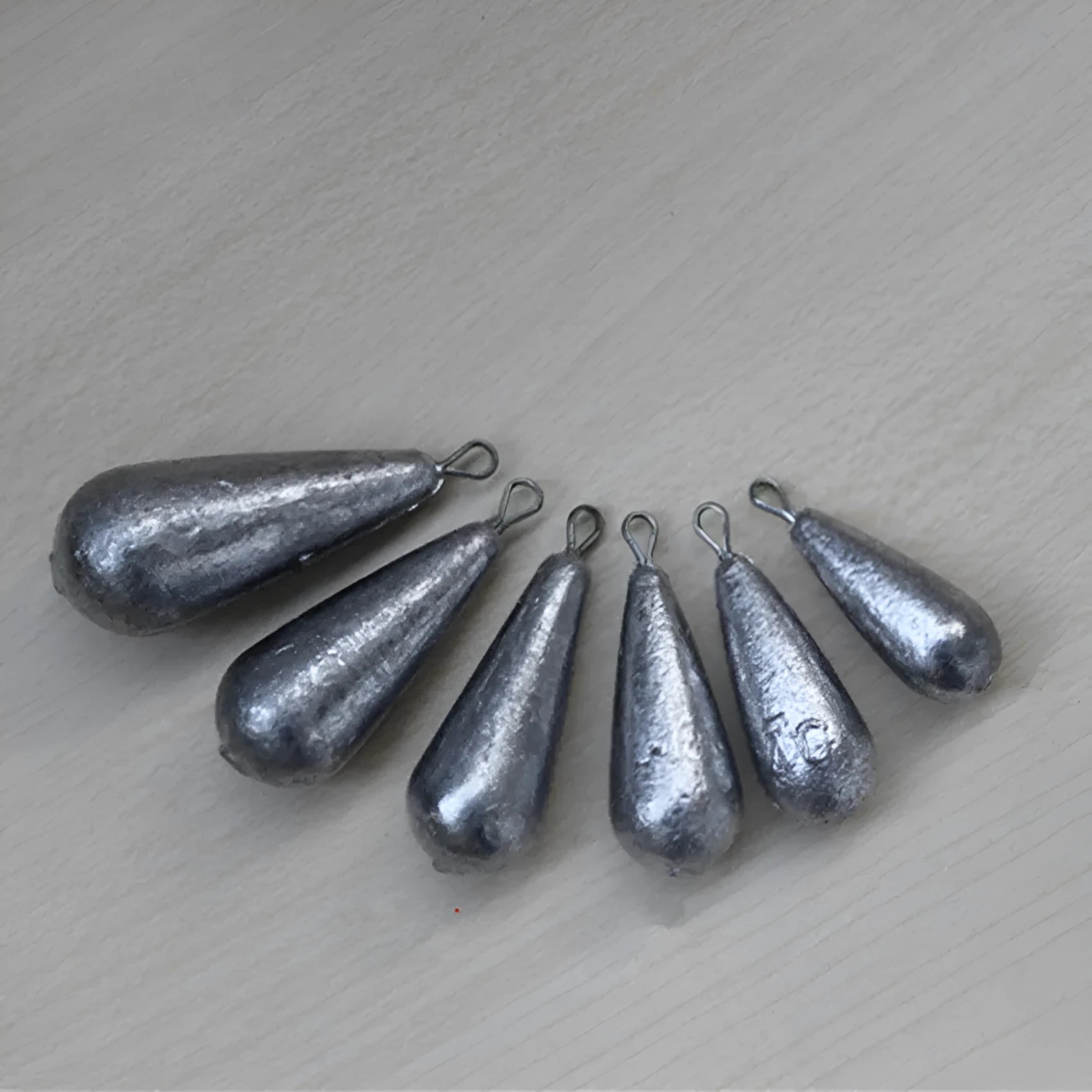 Set of drop-shaped lead fishing sinkers and a Tongxin sinker in various weights from 20g to 50g.