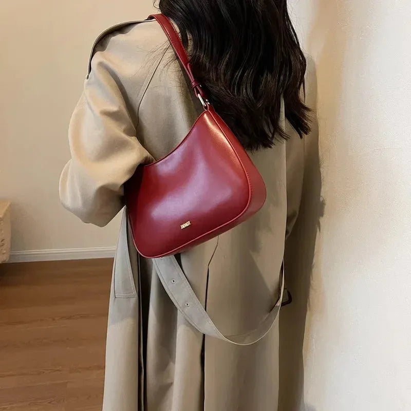 Red underarm shoulder bag in textured faux leather with adjustable strap for crossbody or sling wear