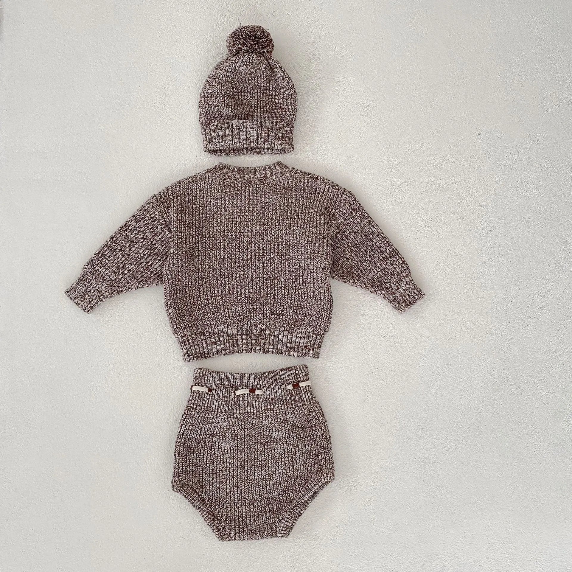 Dark brown knitted three-piece set for infant girl with fur ball hat, blouse, and shorts.