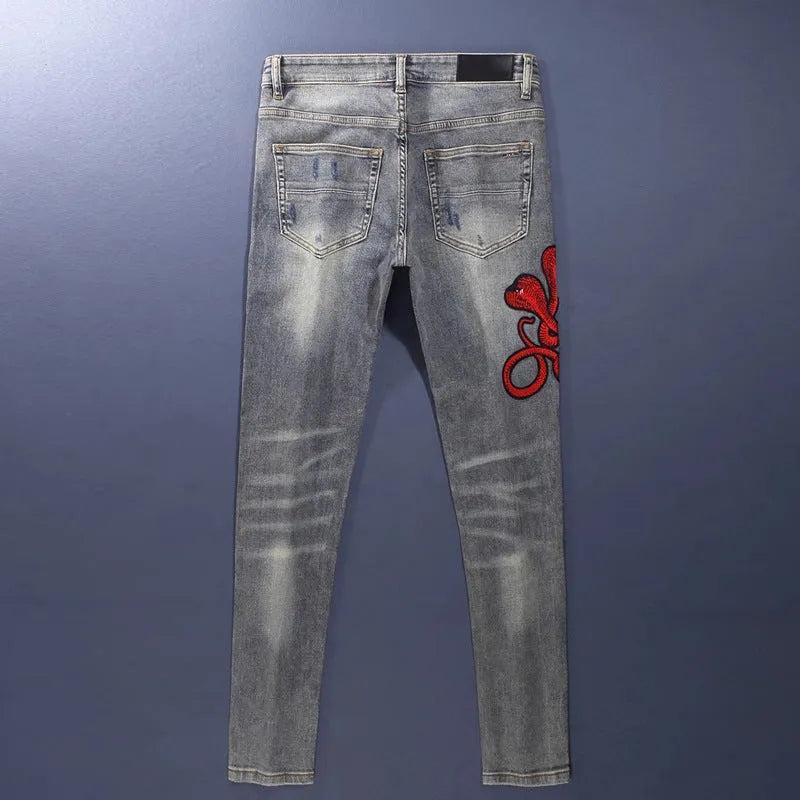 Man wearing slim-fit light blue jeans with distressed knee patches and embroidered back pocket detail.