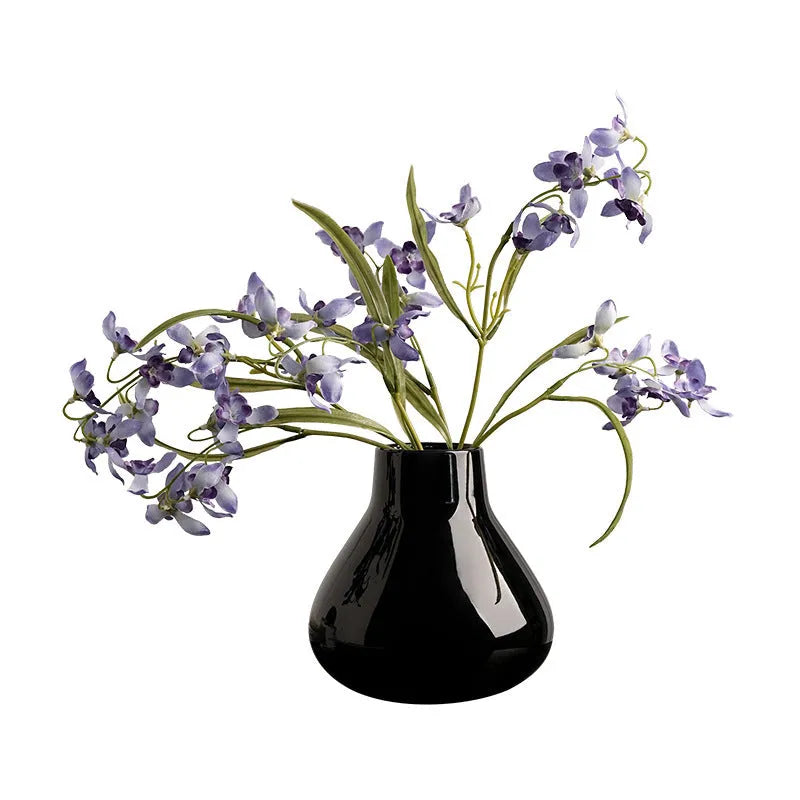 Black ceramic round belly French decorative vase with artificial flower stems on wooden surface