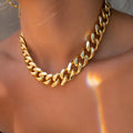 Gold electroplated women's necklace with thick chain and teardrop pendant on a grey background.