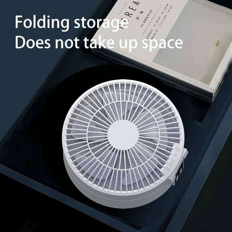 White portable folding electric fan with remote control and warm night light on a desk.