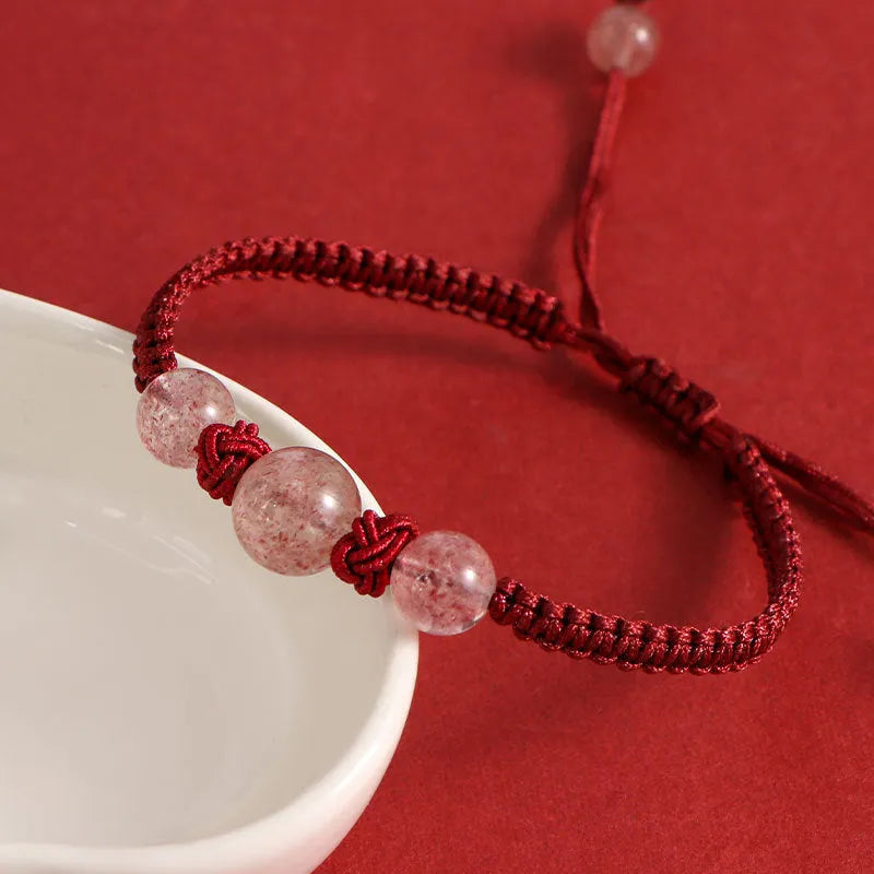A woven red rope bracelet with a natural strawberry quartz bead and an alloy clasp.