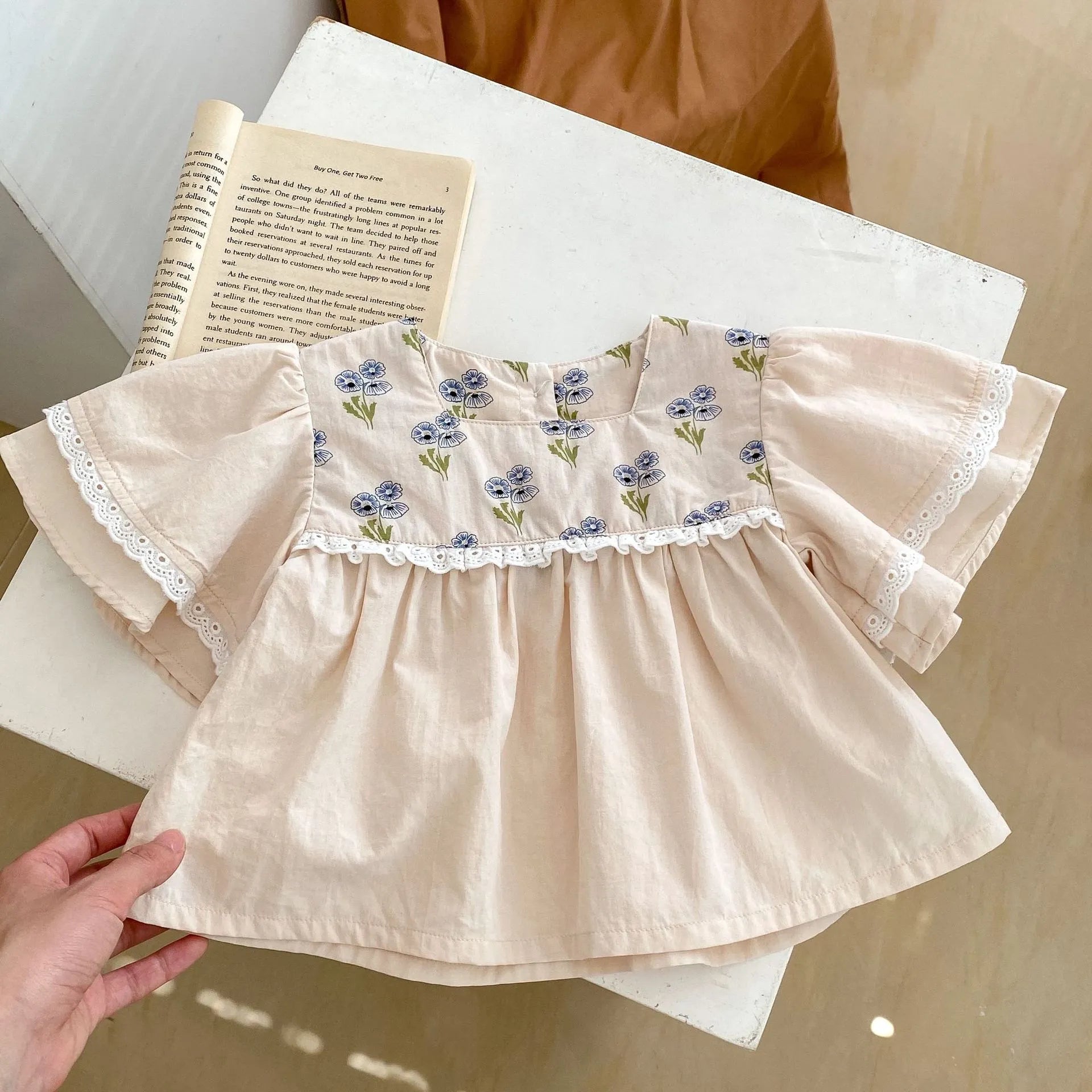Apricot cotton two-piece suit with floral pattern, square collar top, and wooden horn buttons, next to matching bloomer pants.