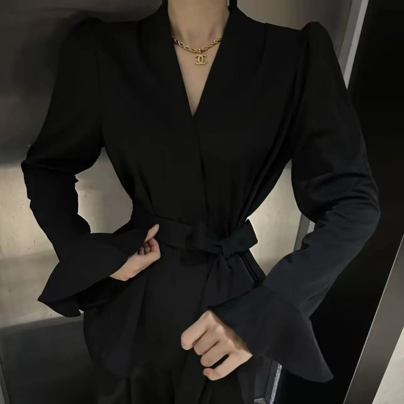 Woman wearing a black tied shirt with a French-style collar and long bell sleeves.
