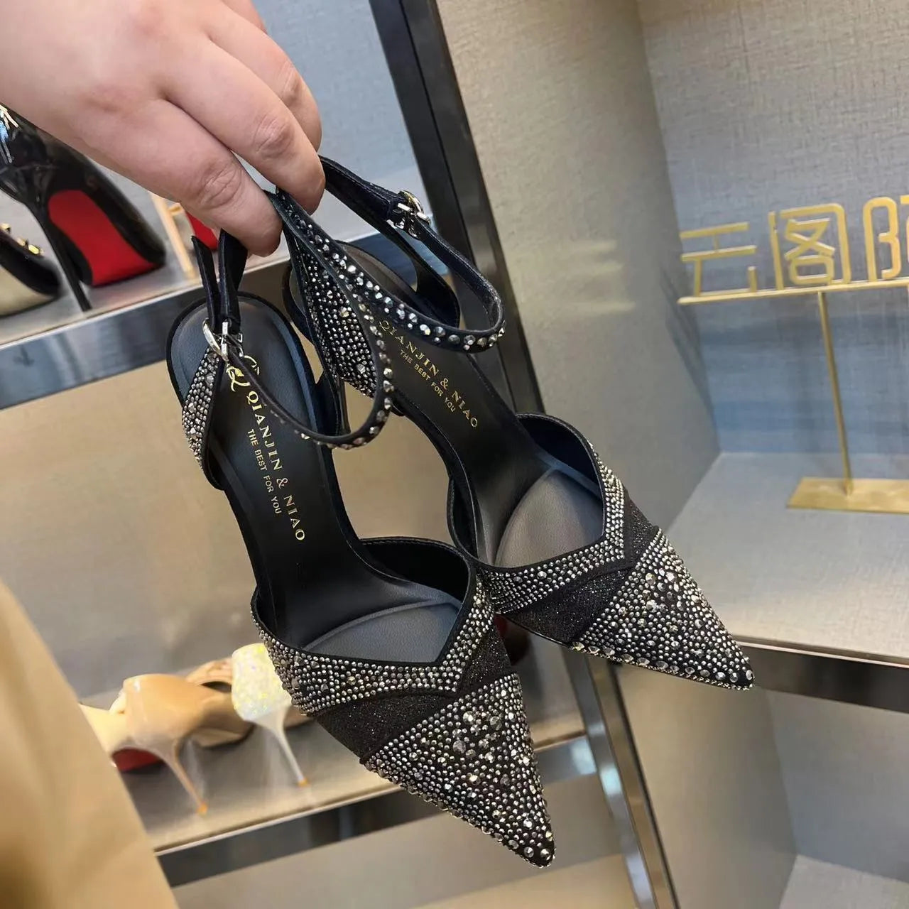 Women's black hollow high heel shoe with red sole and pointed toe, shown next to a silver pair.