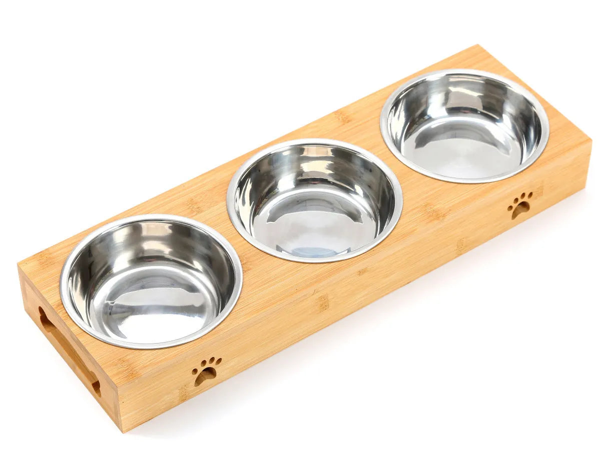 Solid wood elevated pet feeder with stainless steel bowls in a bamboo finish on a wooden floor.