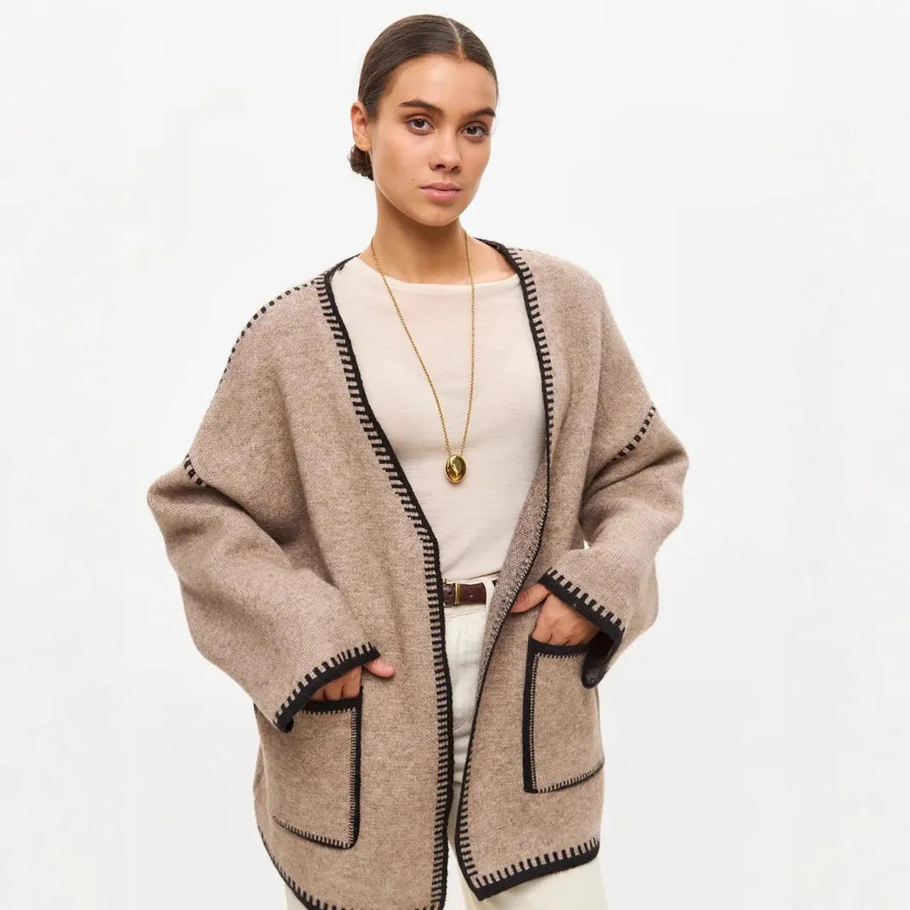 Loose beige knitted cardigan with a lace-up front, worn open over a white top.
