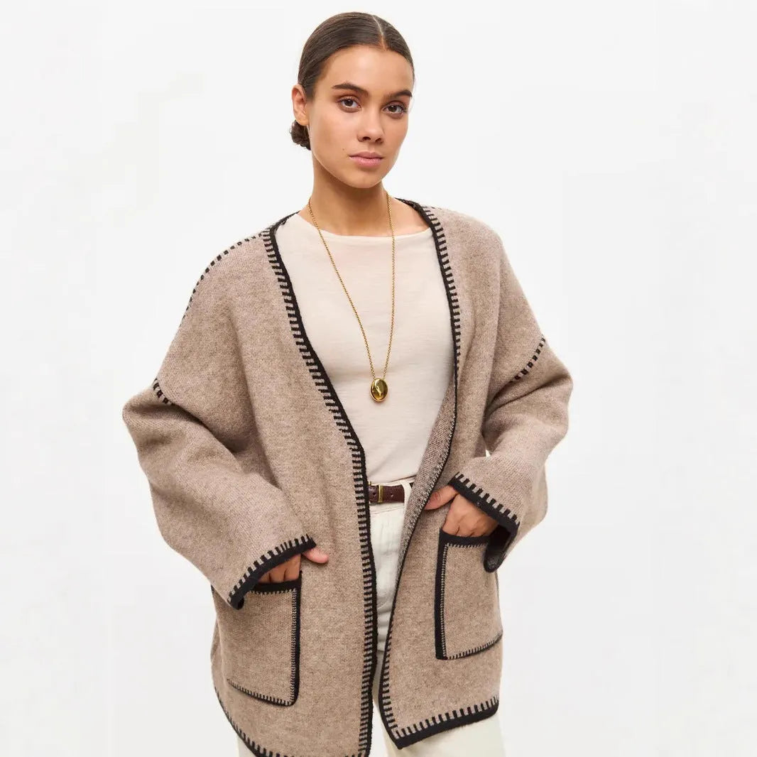Loose beige knitted cardigan with a lace-up front, worn open over a white top.