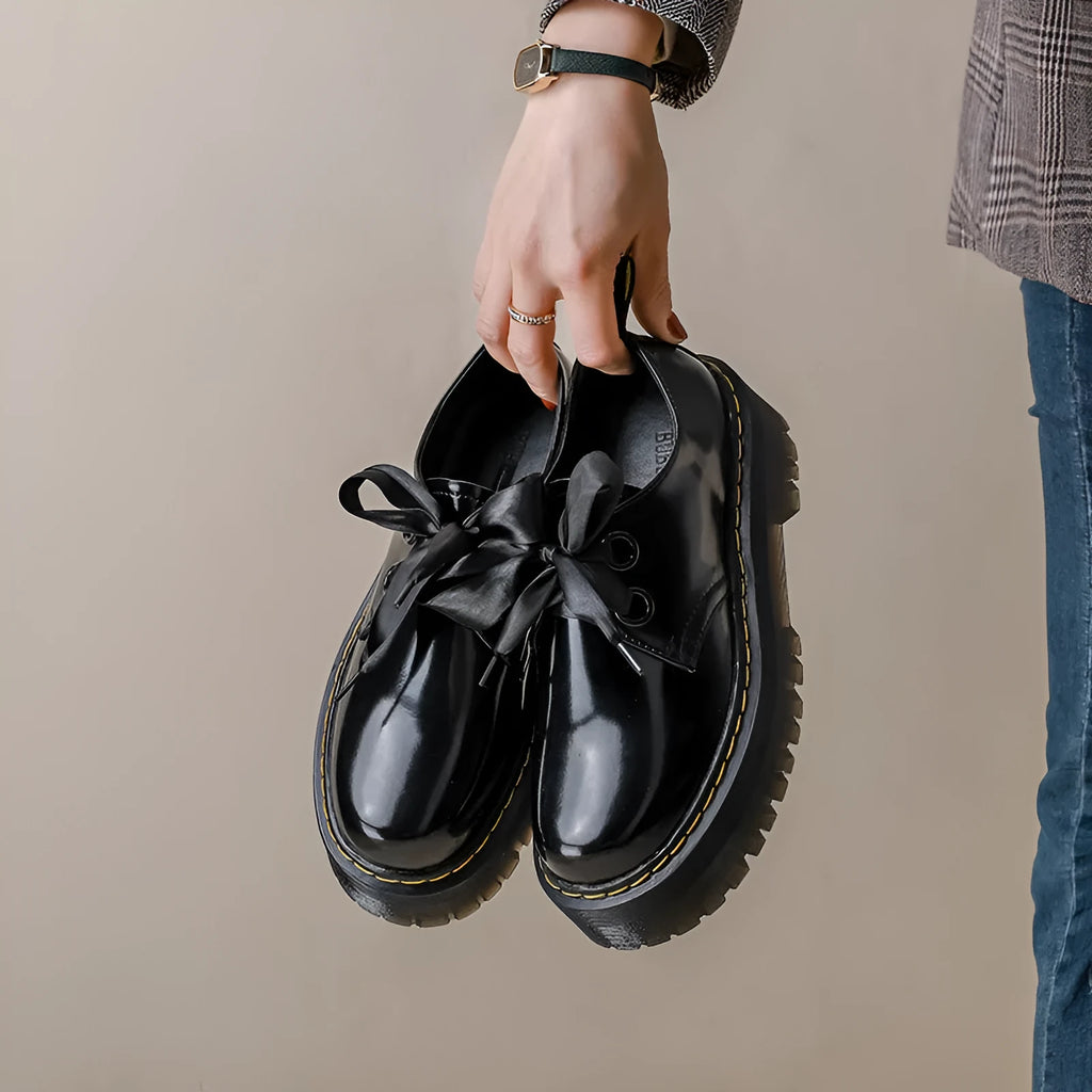 Women's black leather shoes with a thick sole, cross strap, and lace-up closure.