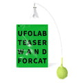 Green cat corner scratcher with plastic base and long teaser stick on a light background