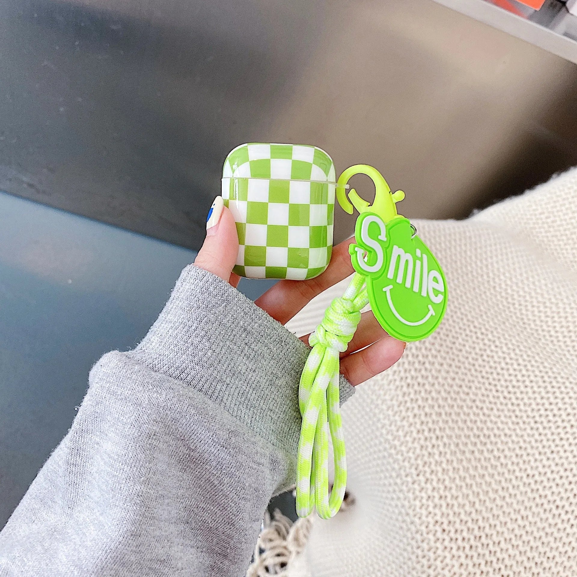 Black and green checkerboard pattern TPU protective case sleeves for Apple AirPods, one with a smiley face lanyard attached.