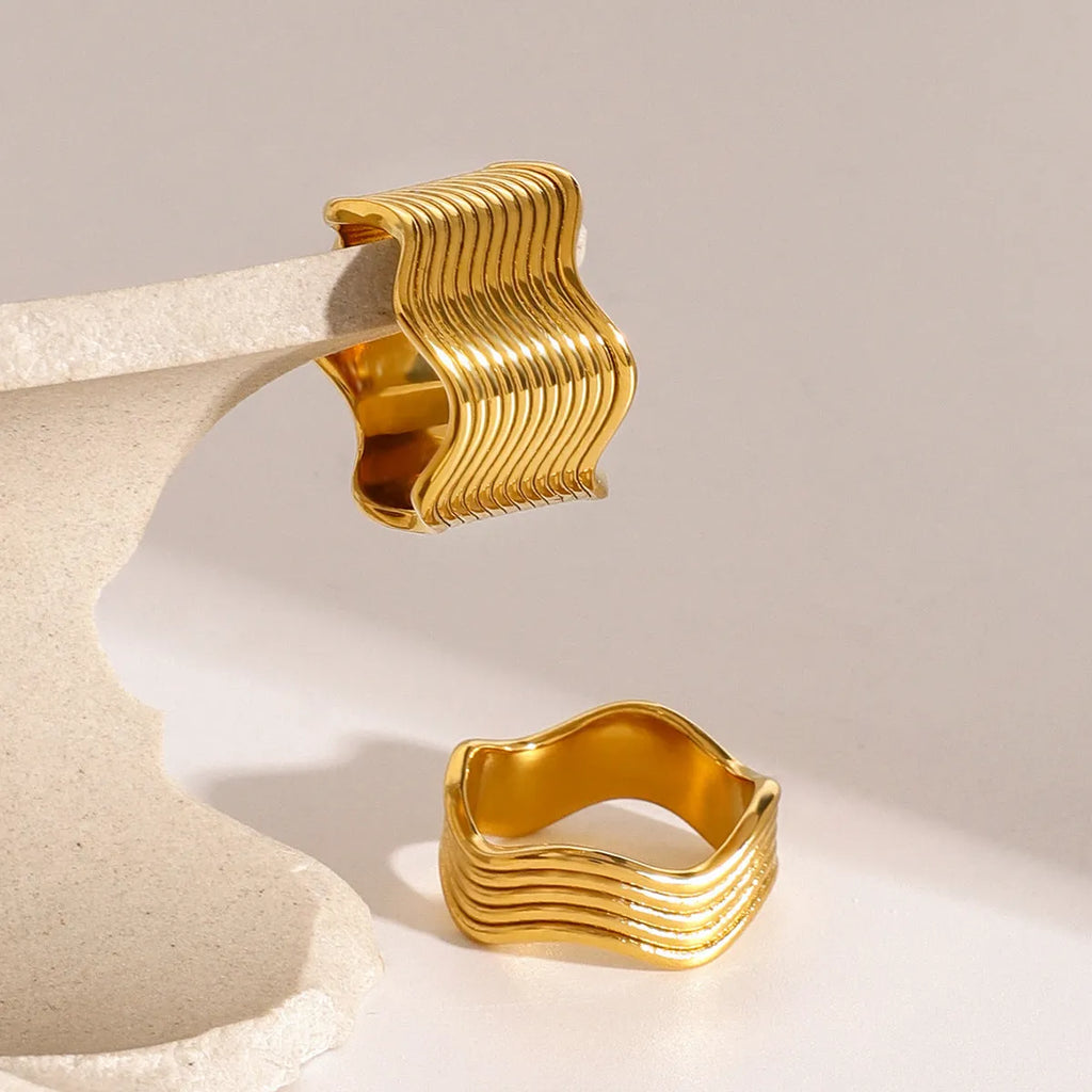 Stainless steel wide band wave ring in geometric Korean style on a plain background.