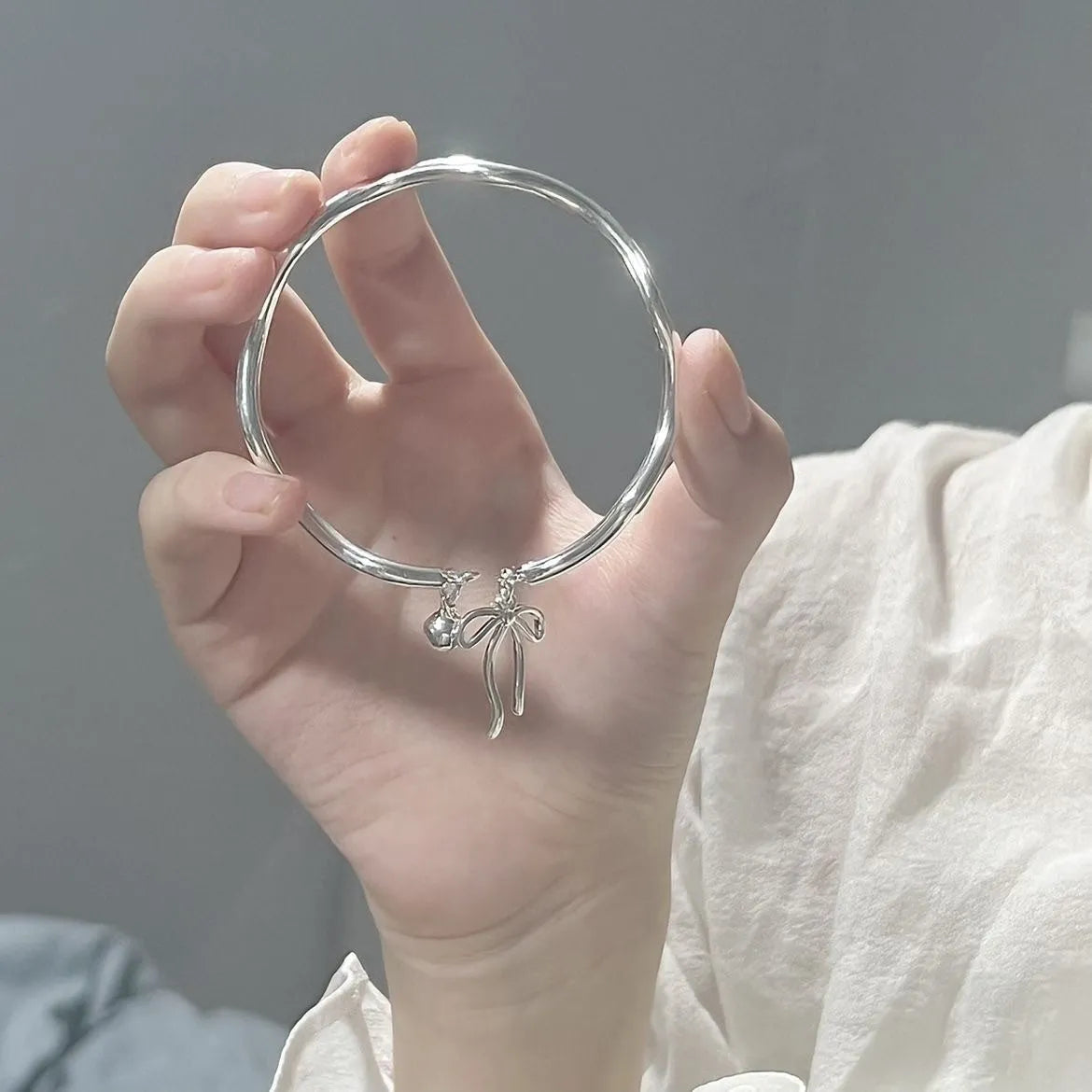 Silver adjustable bangle bracelet with a detailed bow charm and small bell on a wrist.