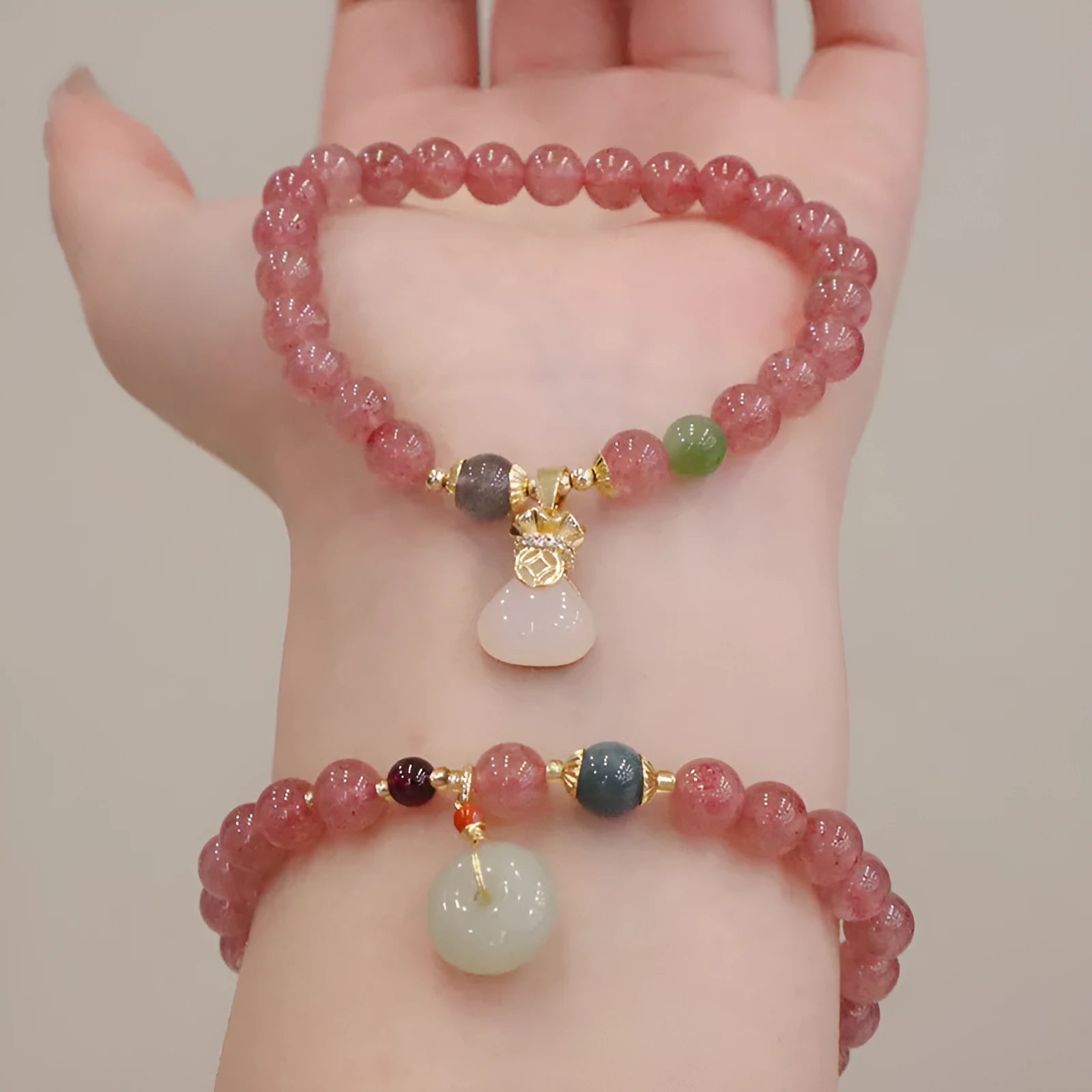 Women's strawberry quartz bracelet with geometric stones, purse charm and lucky bagg charm on wrist