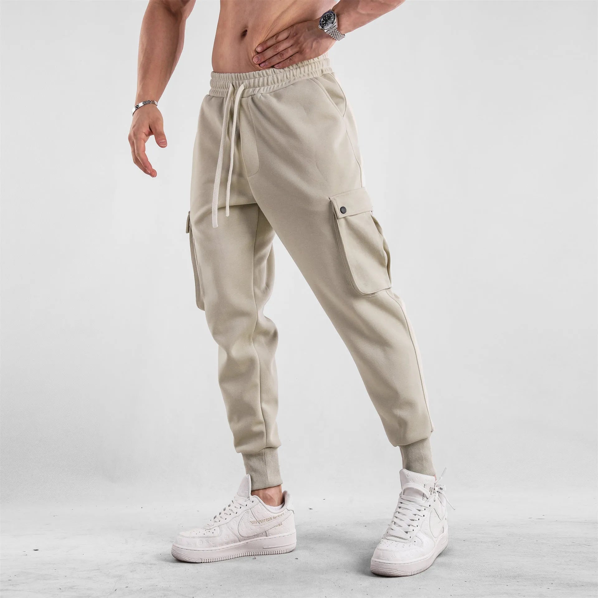 Men's loose-fit beige trousers with ankle ties and multiple pockets, laid flat.