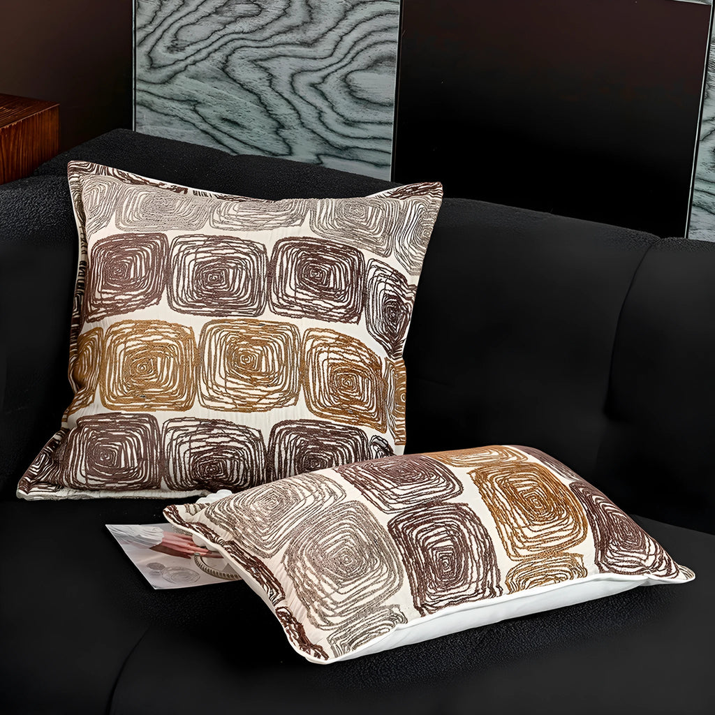 Cream and coffee coloured abstract coil pattern square and waist pillow covers on a sofa.