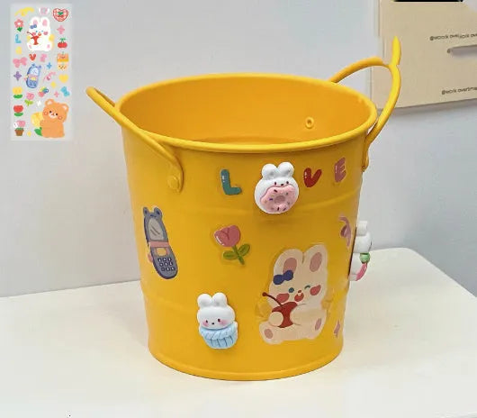 Round metal pen holder in a choice of colours, some with decorative sticker patches, on a wooden desk.