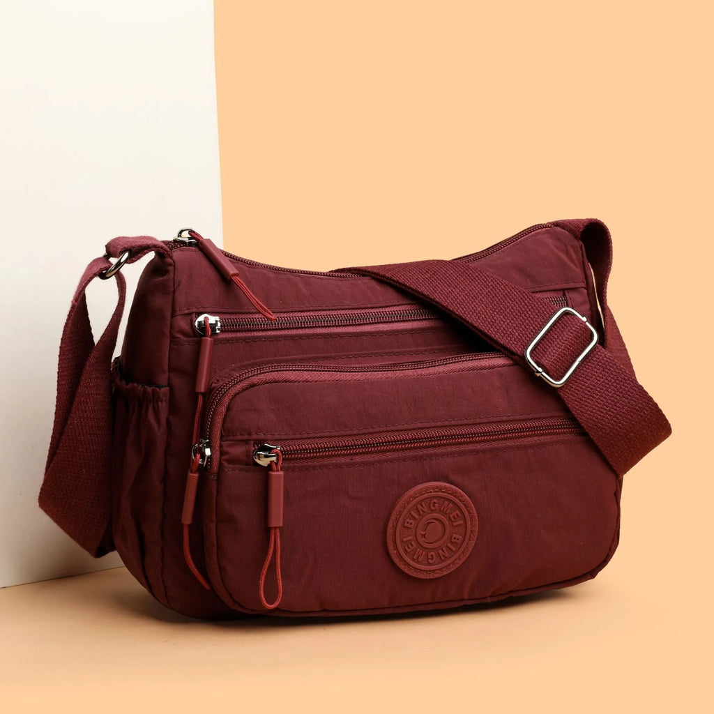 Soft nylon crossbody bag in black, grey, or red with a single shoulder strap and water-repellent finish.