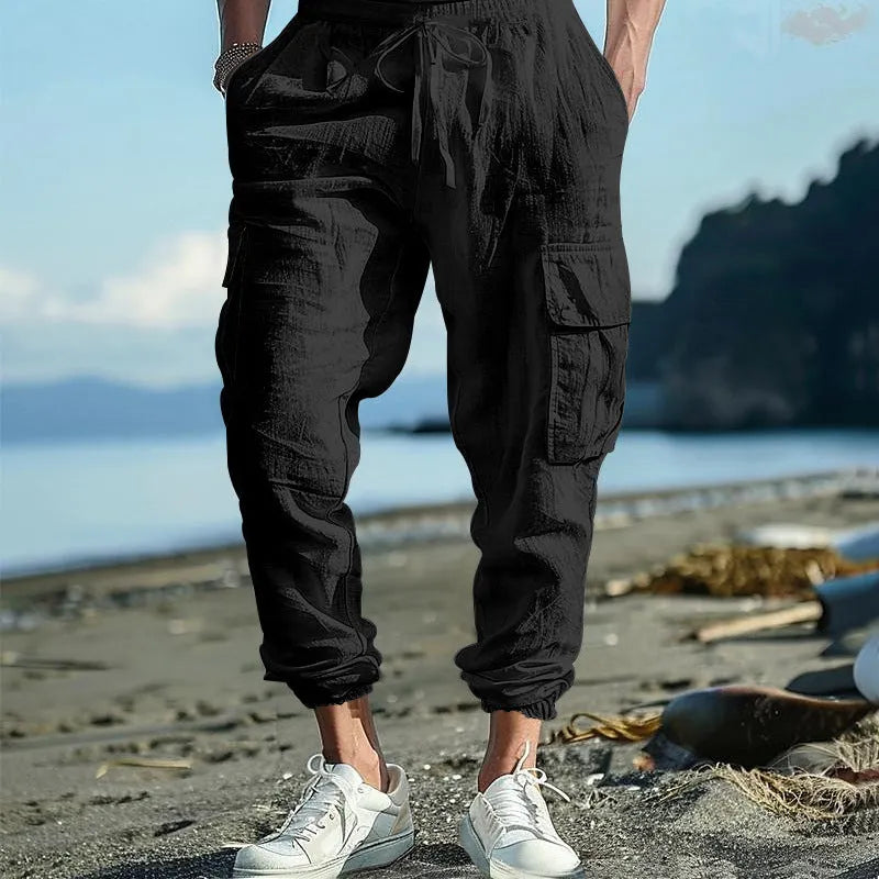 Men's loose-fit linen trousers with ankle ties, multiple pockets, and a drawstring waist in a solid colour.