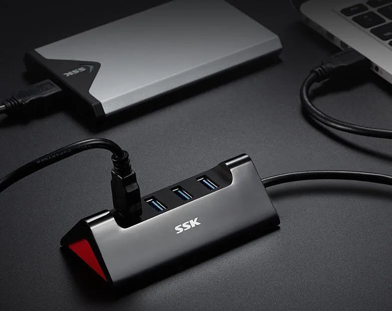 Black plastic USB hub with four USB-A ports and a Micro USB power port on a desk.