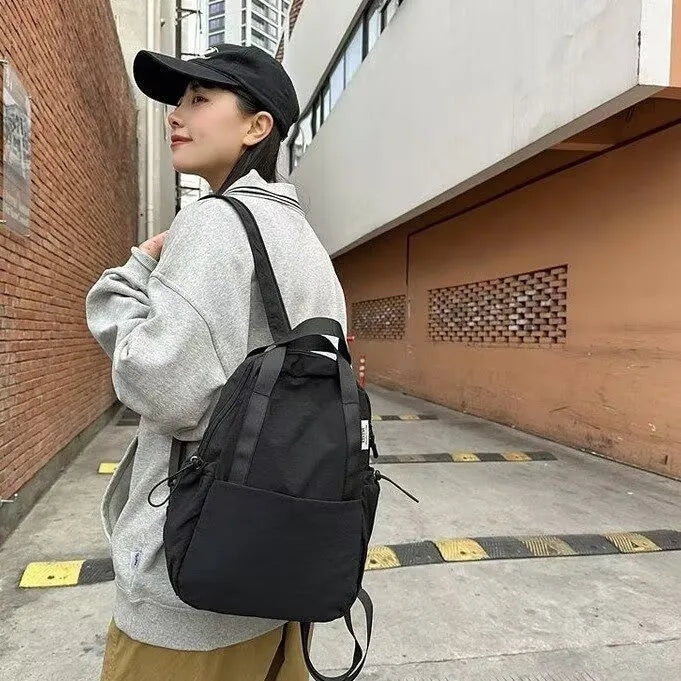 Simple solid colour nylon backpack in black on a neutral background, showing curved shoulder straps and top lock.