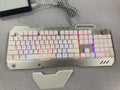 Black wired gaming keyboard with RGB backlight, phone holder, pen tray, and magnetic wrist rest on a desk