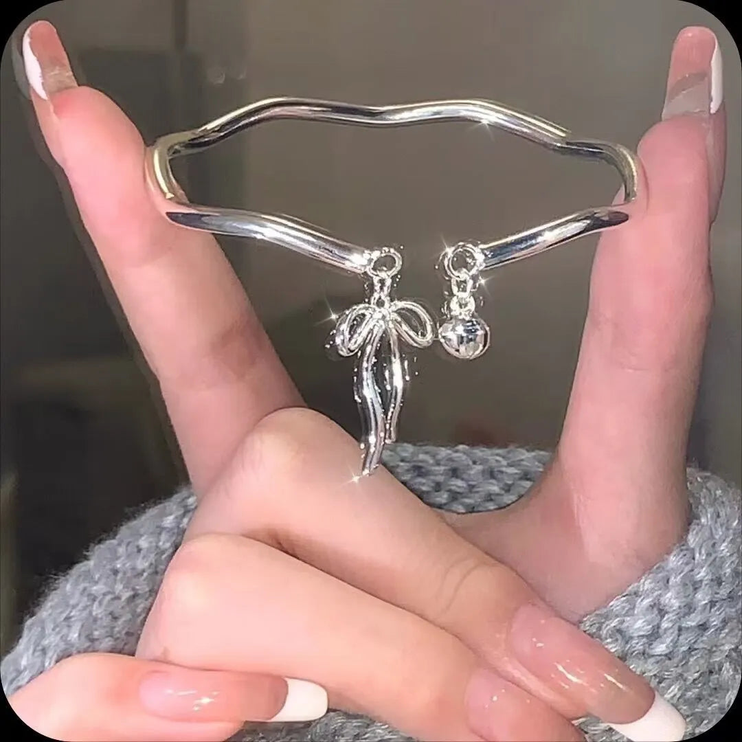 Silver adjustable bangle bracelet with a detailed bow charm and small bell on a wrist.