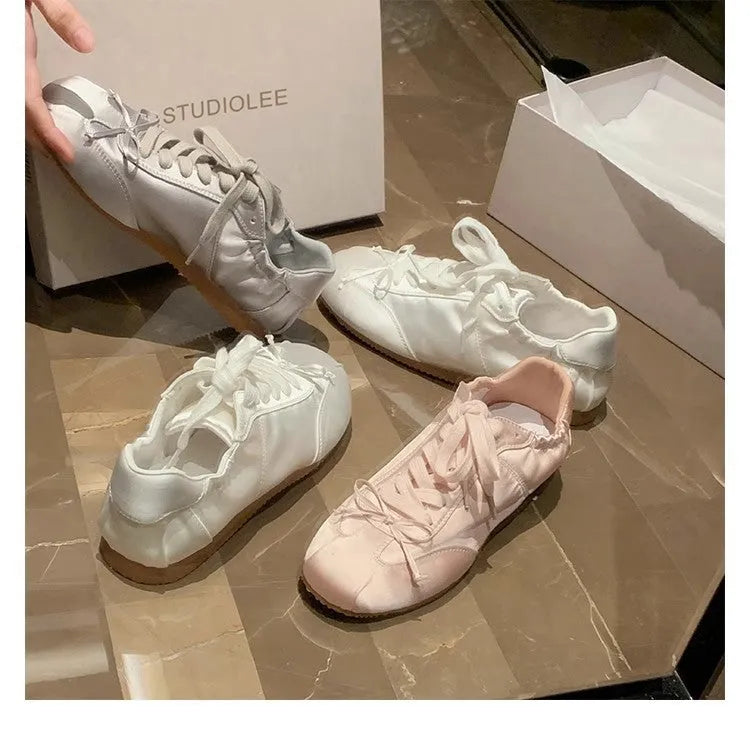 Women's satin ballet flats in champagne pink with round toe and front lace-up closure.
