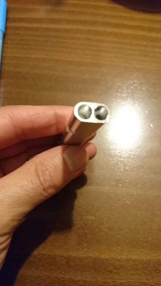 A silver or gold coloured aluminium alloy survival whistle with two holes on a grey background.