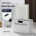 Dark gray automatic dental floss box with USB charging port and pop-up floss dispenser.