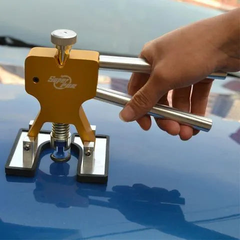 Car dent removal kit with gold puller, rubber tabs, glue gun, and shovel scoops on a workbench