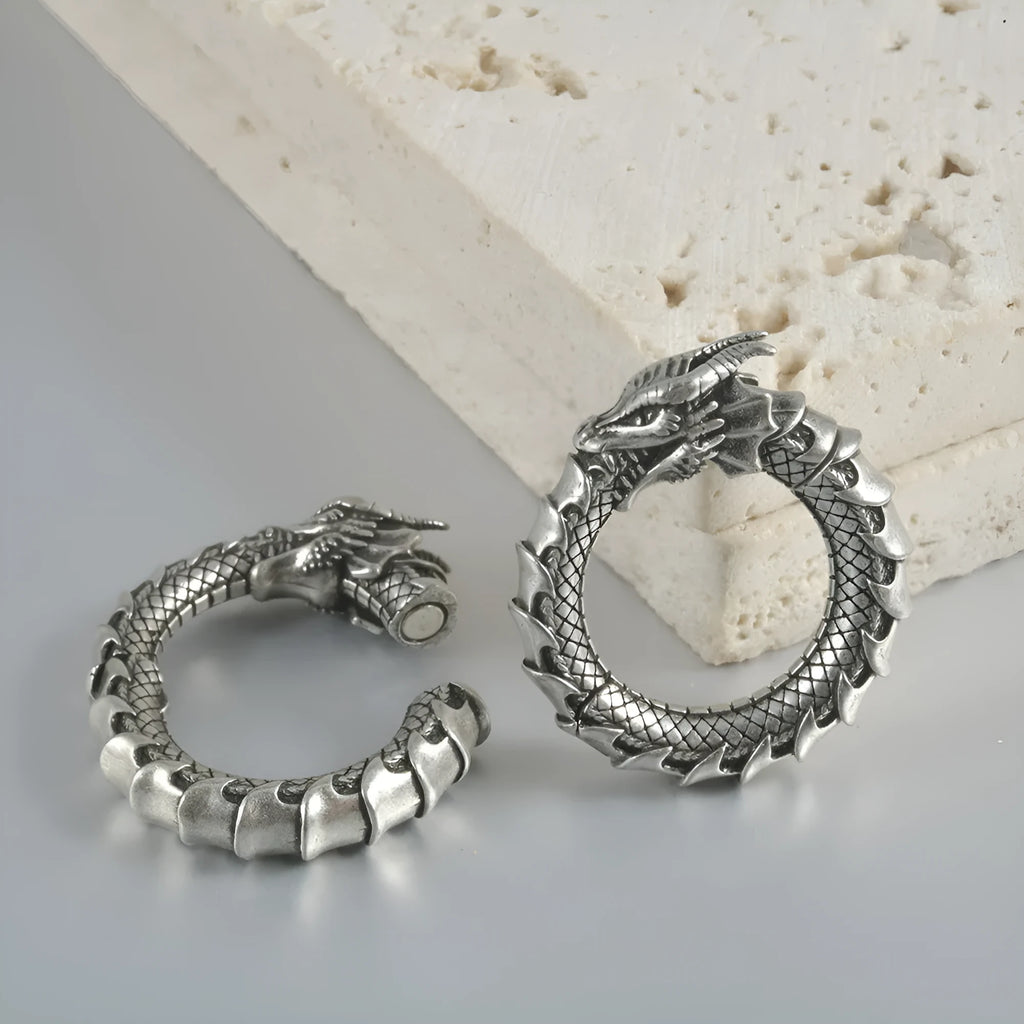 Pair of large antique silver dragon-shaped geometric ear cuffs with hollow-out detail on a plain background.