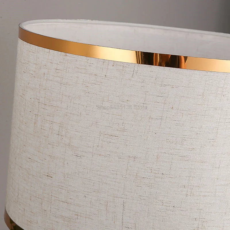 Iron table lamp with a white fabric shade and a push button switch on a wooden table.