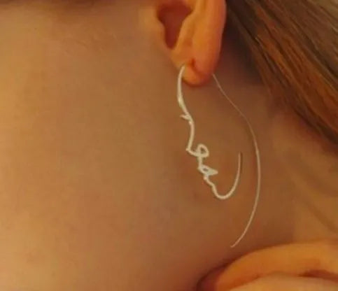 Creative abstract face contour earrings in metal gold finish on a white background