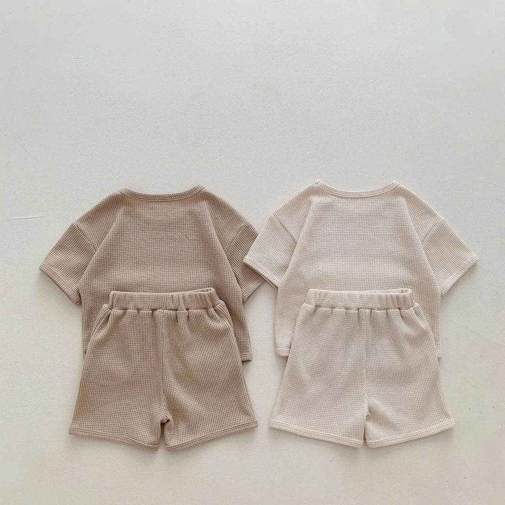 Unisex baby summer suit with bear print cotton top and beige shorts on a neutral background