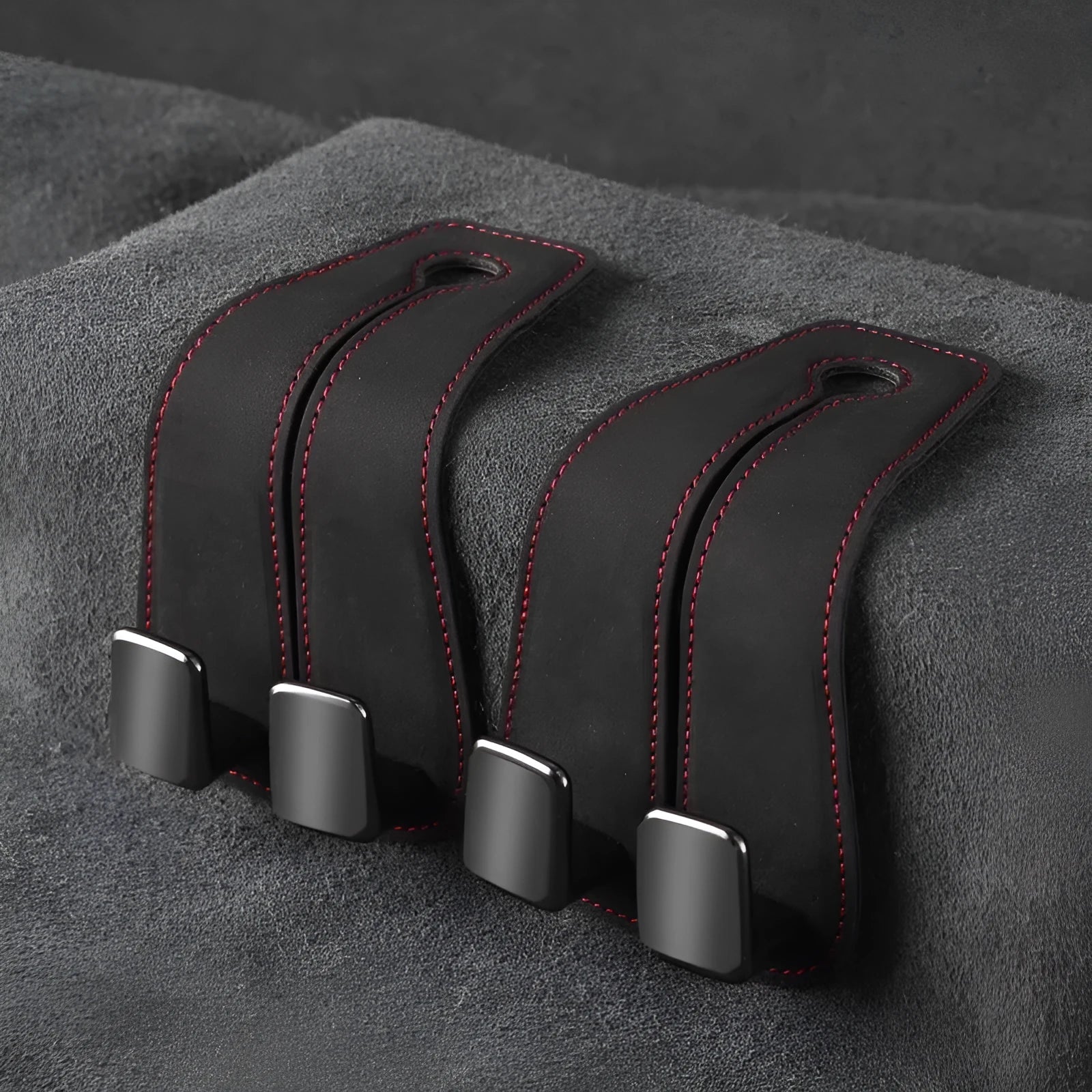 Black car seat hook with suede padding and flip-back design mounted on a grey car seat