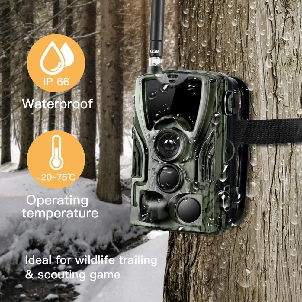 Green outdoor trail camera with lens and infrared LEDs, shown with belt strap for mounting on a tree.