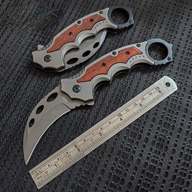 Folding claw knife with grey titanium blade and sour branch wood handle on a surface