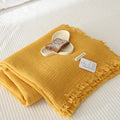 Cotton four-layer gauze blanket with tassel trim in avocado green colour, laid flat.