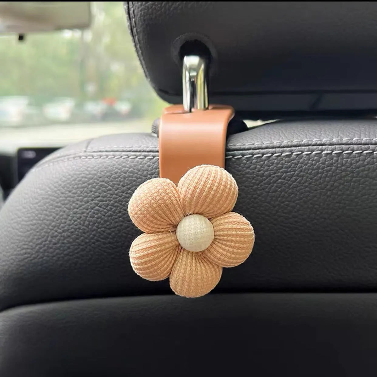 Khaki-coloured plastic car seat hook with a small decorative flower for storage.