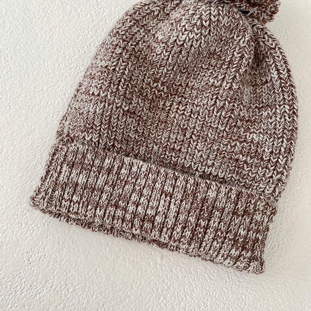 Dark brown knitted three-piece set for infant girl with fur ball hat, blouse, and shorts.