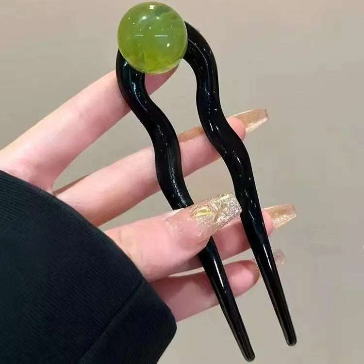 A set of U-shaped acrylic hair barrettes with a ball detail in beige, caramel, dark grey, and green colours