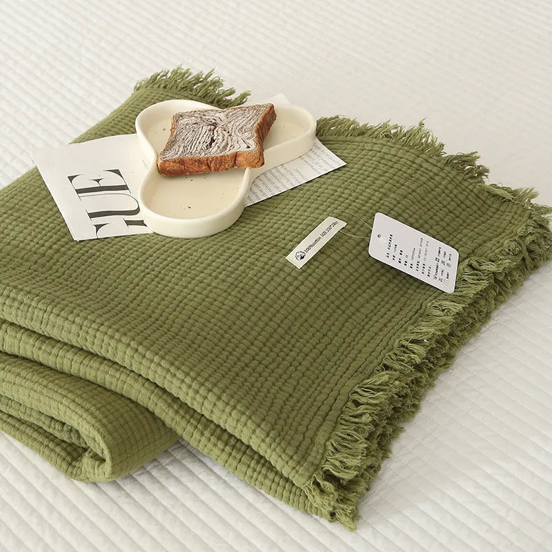 Cotton four-layer gauze blanket with tassel trim in avocado green colour, laid flat.