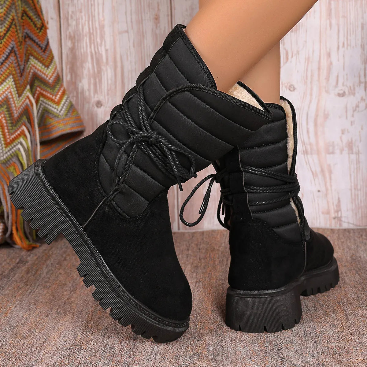 A pair of women's chunky heel snow boots in suede with a lace-up front and fleece lining, shown in black.