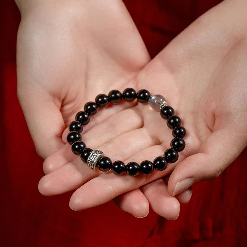 Obsidian bracelet with 8mm beads and a Tibetan zodiac charm on a wrist.