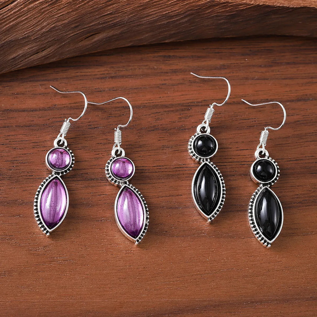 Close-up of geometric vintage pendant earrings in black and purple with a metallic shine.