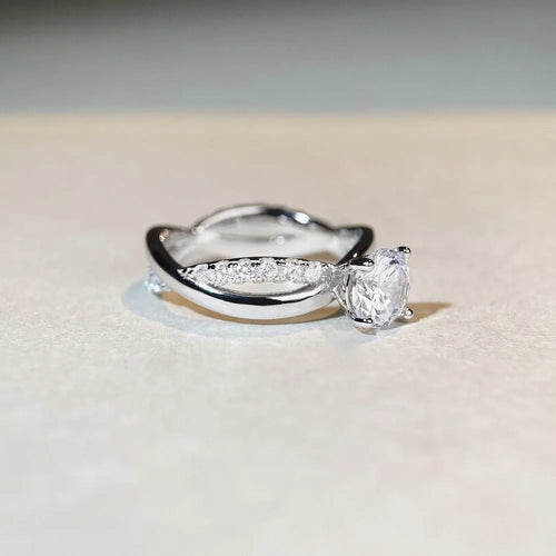 Silver ring with a 1 karat moissanite stone in a four-claw setting on a twisted geometric cross band.